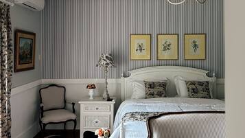 A bedroom with a bed, a chair, a nightstand, a lamp, and a chandelier.