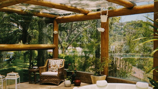 Una estructura de pérgola de madera con un jacuzzi y zona de estar, rodeada de abundante vegetación y árboles.