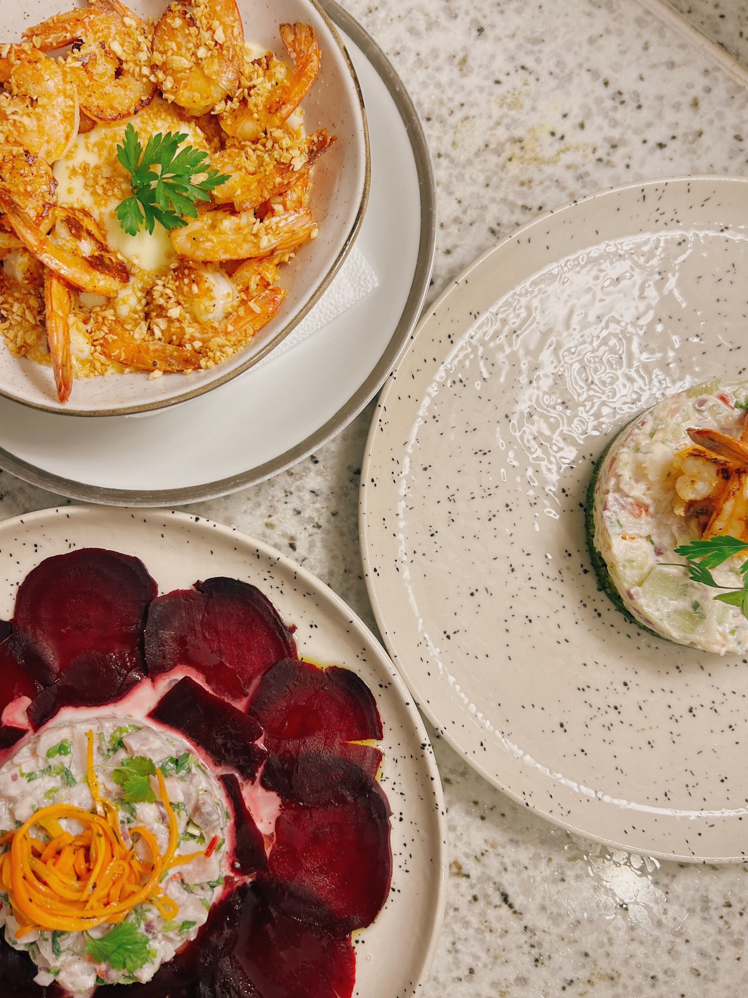 Tres platos de comida: camarones, ensalada de remolacha y un guiso cremoso con adorno.