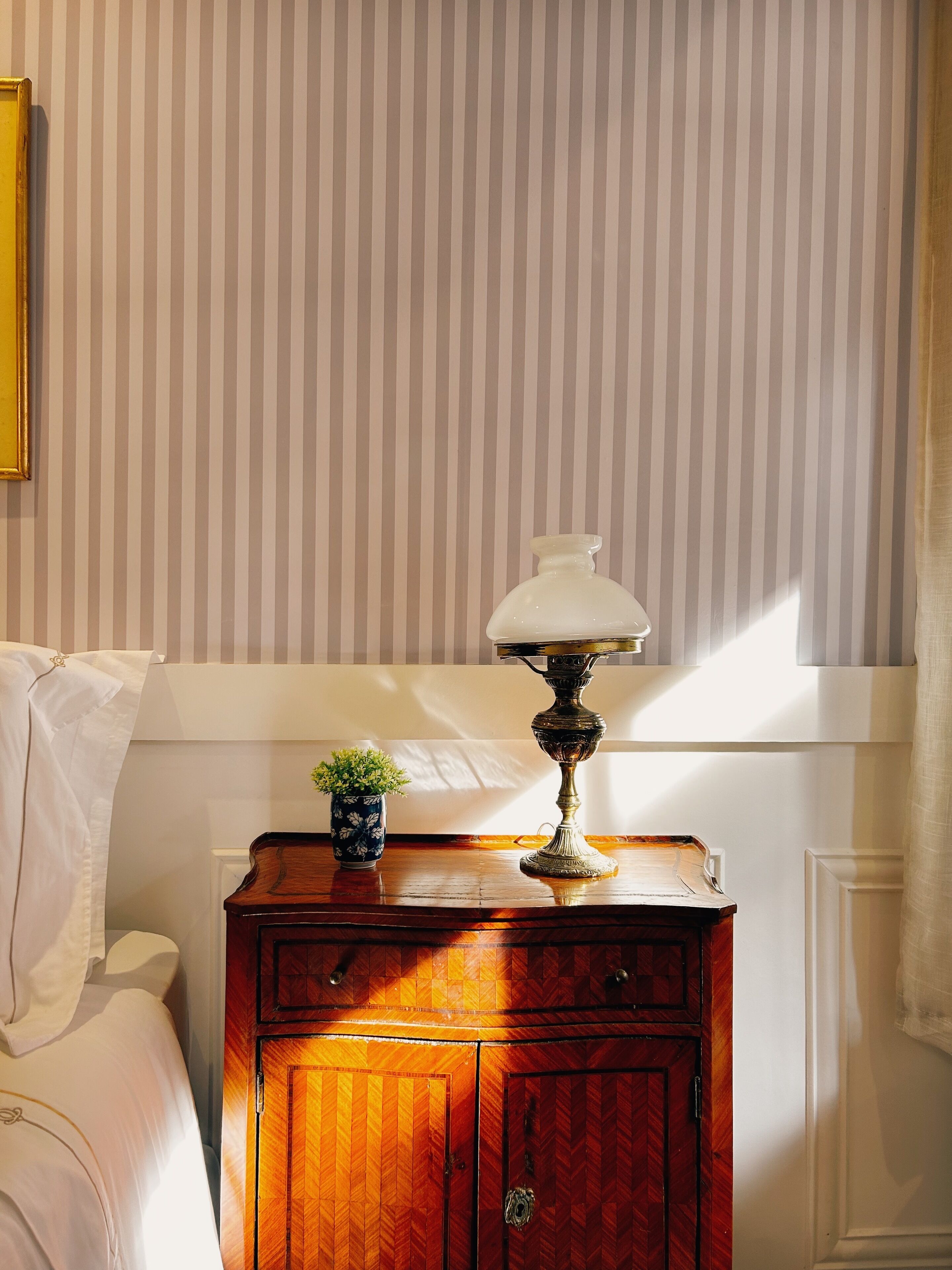 Una habitación con una cama, un armario de madera con una lámpara y una pared a rayas.