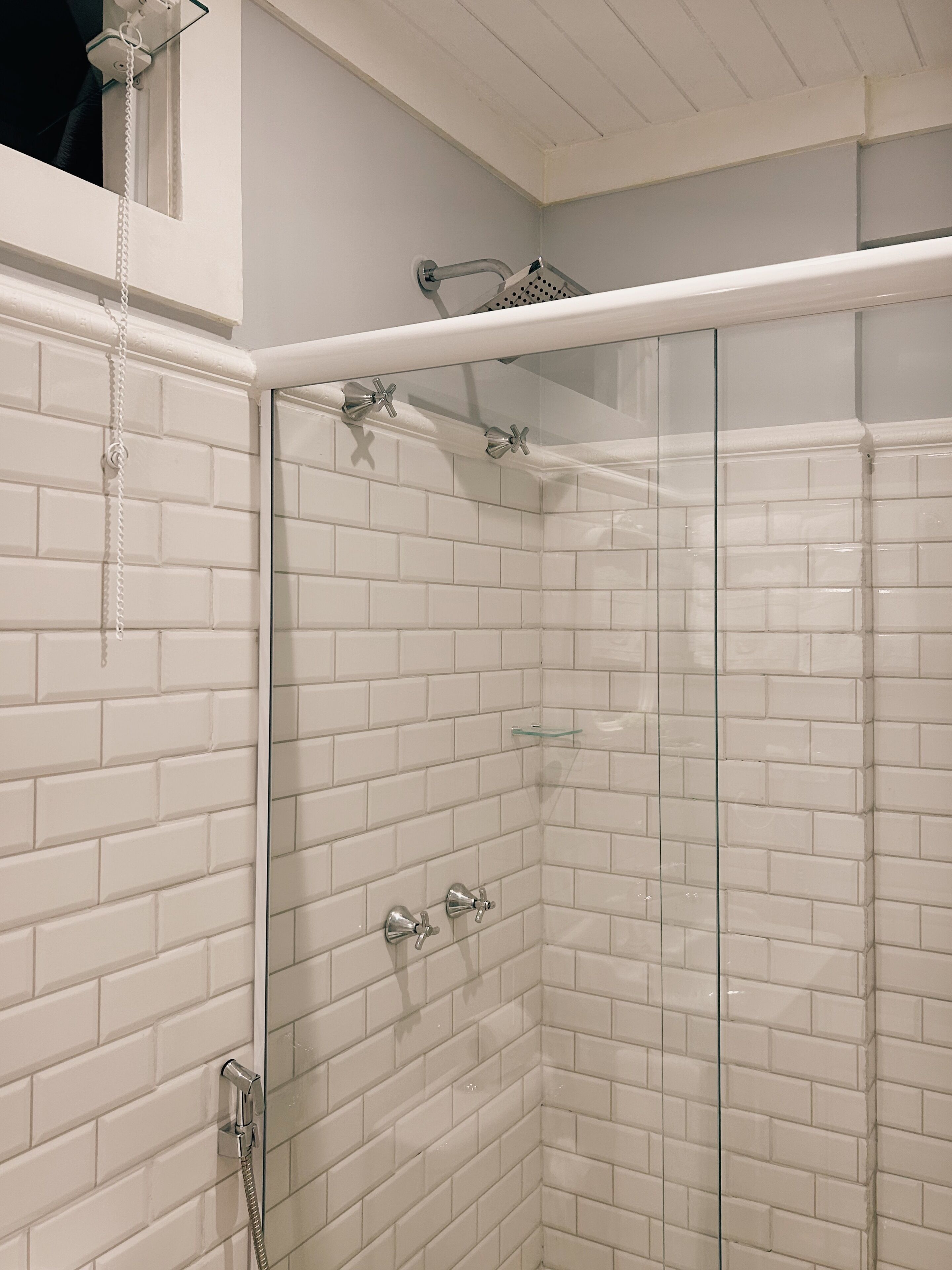 A glass-enclosed shower with white tiled walls and a white ceiling.