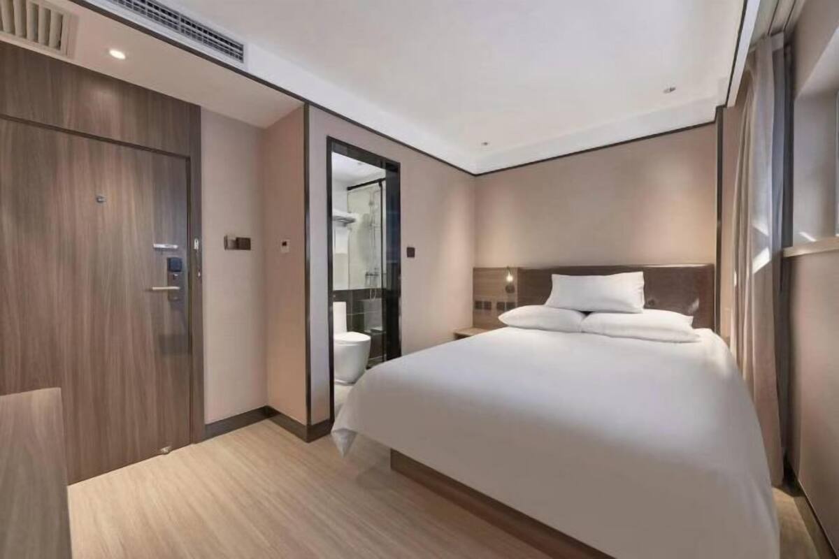 A modern hotel room with a large bed, a walk-in closet, and a bathroom with a glass shower.