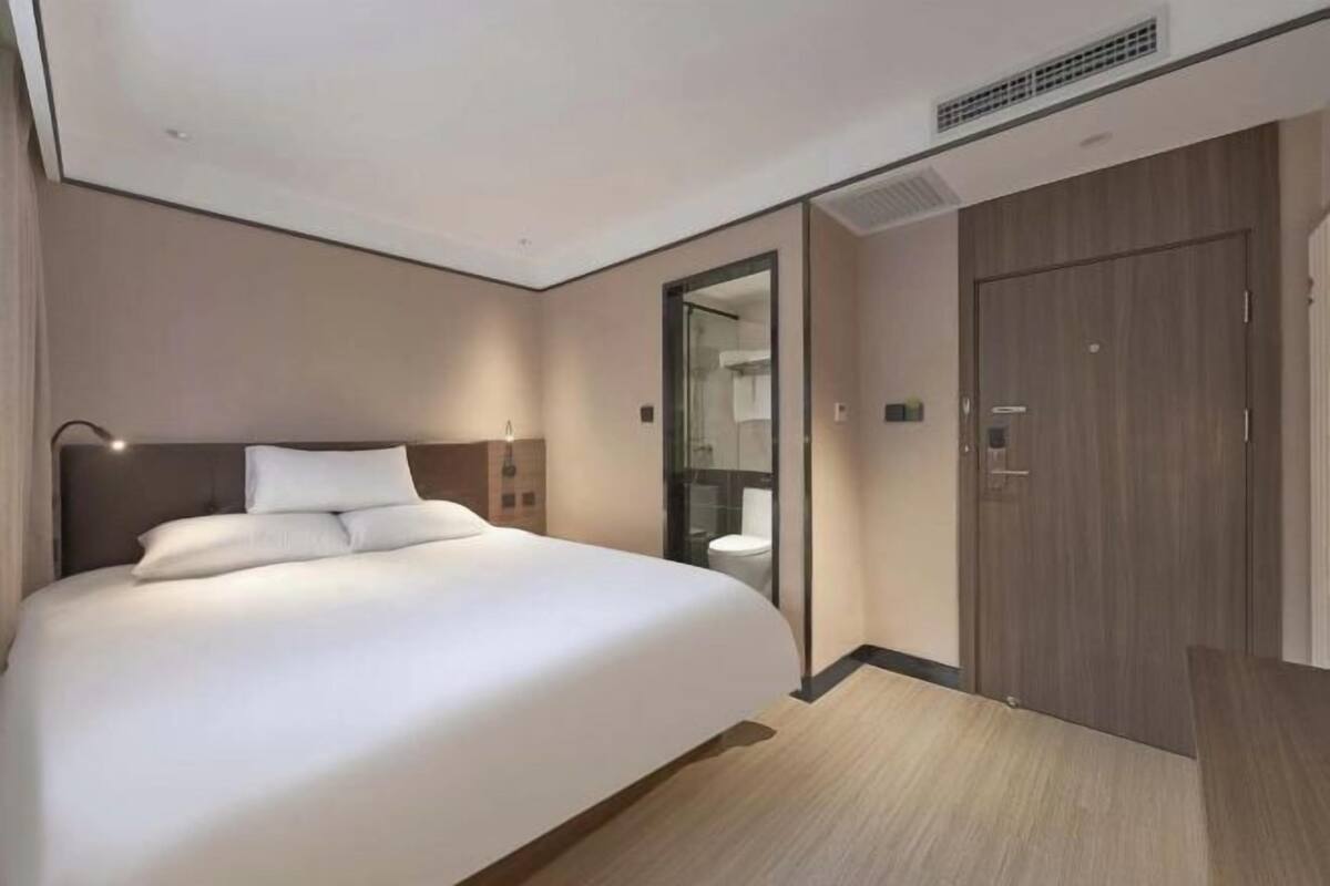 A modern hotel room with a large bed, a separate bathroom, a wooden wardrobe, and a glass partition.