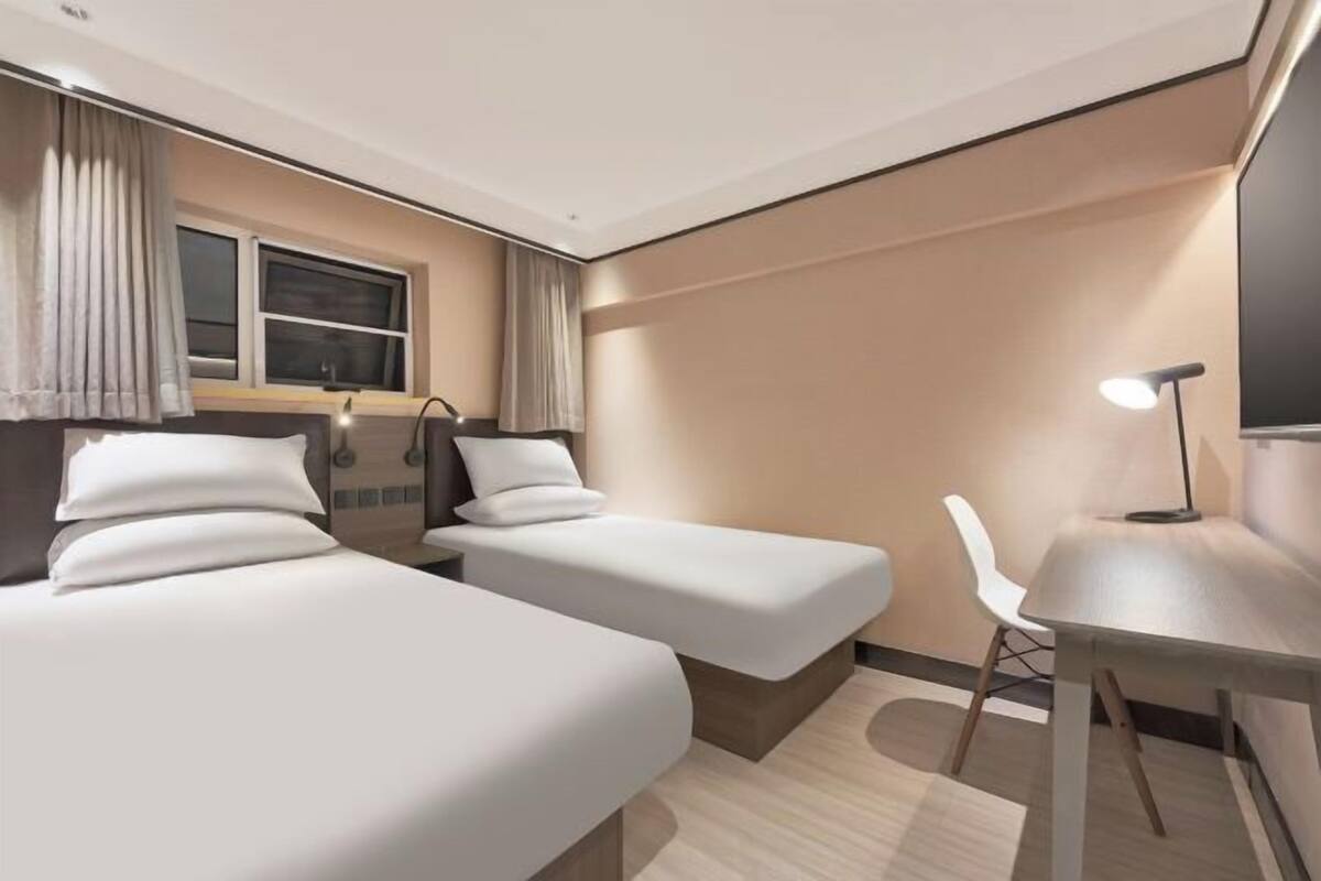 A hotel room with two beds, a desk, a chair, a TV, and a window with curtains.