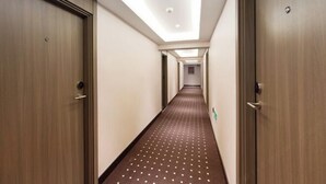 Ein Hotelgang mit Holztüren, einem gemusterten Teppich und eingelassener Deckenbeleuchtung.