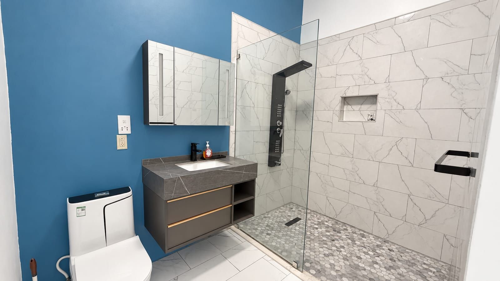 A modern bathroom with a blue wall, a marble-tiled shower, a white sink, and a dark-toned vanity.