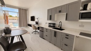 A modern kitchen with grey cabinets, a black sink, and a microwave. There is a dining area with a table and chairs. - P ÀRIS Villas Business Suite (Gros Islet)