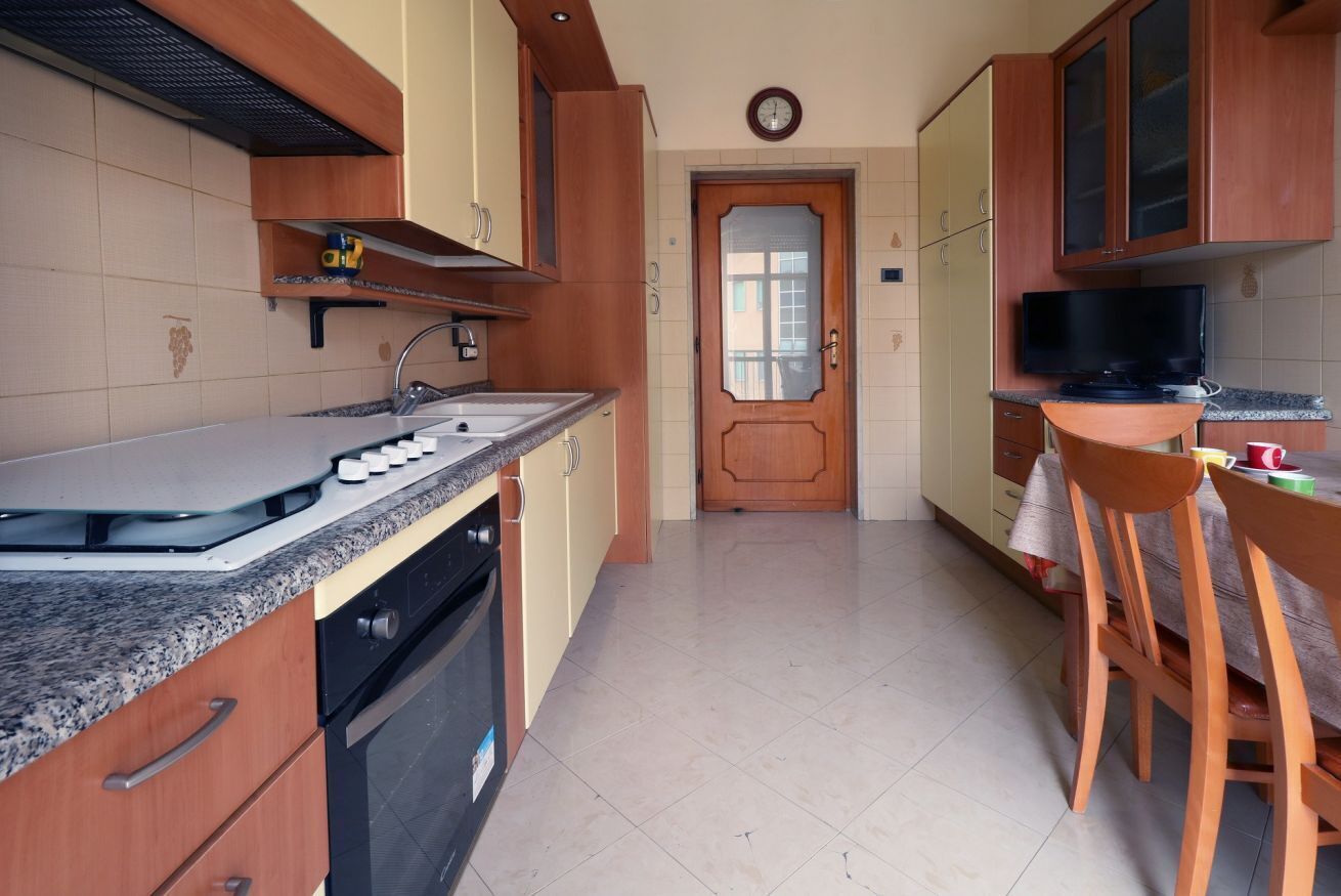 Una cucina con un piano di lavoro in granito, mobili in legno, forno integrato e zona pranzo con tavolo e sedie.