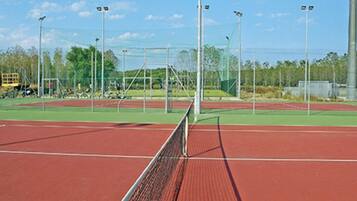A tennis court with a net, surrounded by green areas and trees.