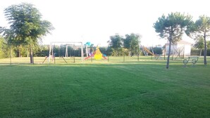 A grassy park with playground equipment including swings and a climbing structure. - BORGO SAN BASILIO: MOONLIGHT HOUSE - CON PISCINA E ANIMAZIONE DIURNA E SERALE (Pisticci)