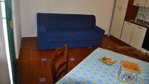 Une petite cuisine avec un canapé bleu, un sol carrelé et une table recouverte d’une nappe à carreaux.