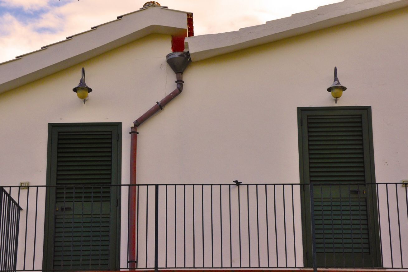 A building facade with two green shutters, a red pipe, and a black metal fence.