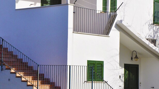 Un immeuble à plusieurs étages, doté d’un escalier, de volets verts et d’un balcon avec une rambarde en métal.
