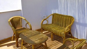 Un balcón con mobiliario de mimbre, incluyendo una silla, un sofá y una mesita.