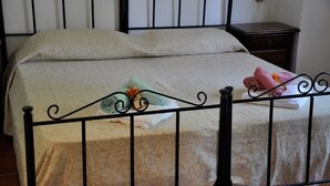 Uma cama com colcha florida, cabeceira de metal e mesa de cabeceira com abajur.