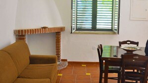 Uma sala de estar com sofá, uma mesa de jantar com cadeiras, uma janela com persianas e uma lareira.