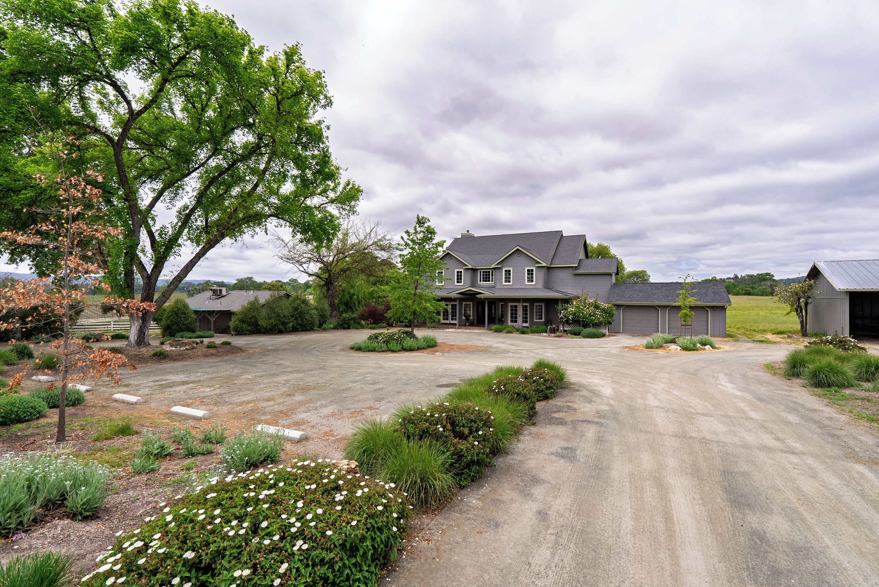 A large house with a driveway leading to a garage, surrounded by well-maintained landscaping and trees.