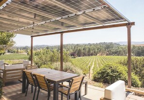 An outdoor patio with a table and chairs, a pergola with solar panels, and a vineyard view. - Hive Vista @Castoro | Vineyard View Stay + EV (Templeton)