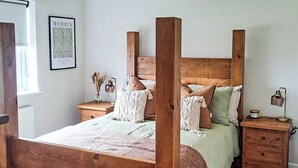 Una cama con dosel, un cabecero de madera, una mesita de noche con una lámpara y un cuadro en la pared.
