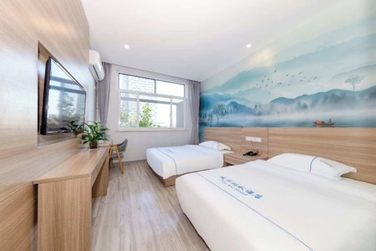 Habitación de hotel con un escritorio de madera, dos camas, un ventanal grande y un mural con un paisaje.