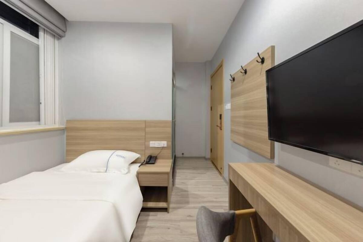 A hotel room with a bed, bedside table, TV, and a wardrobe.