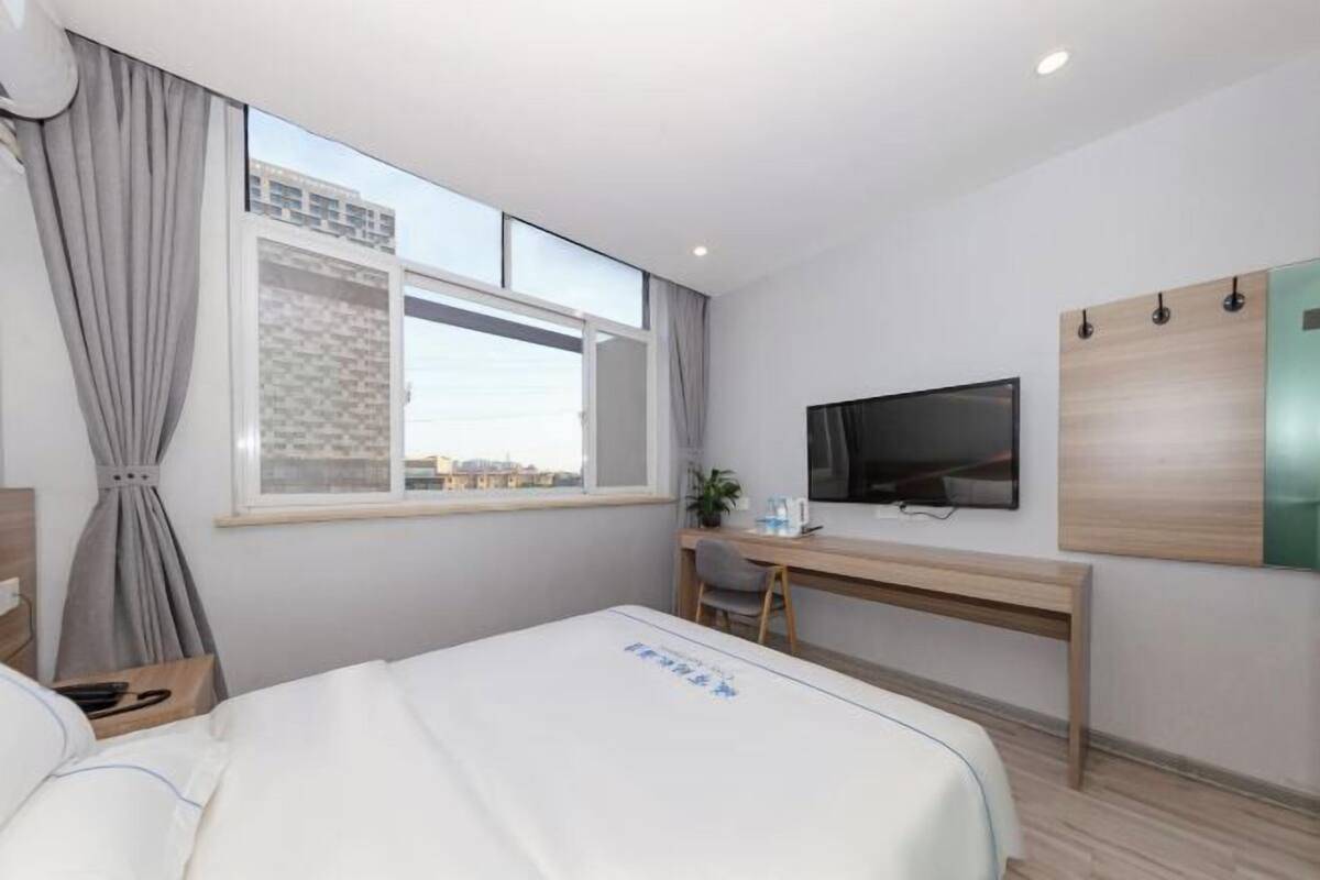 A hotel room with a bed, a desk, a TV, and a window with curtains.