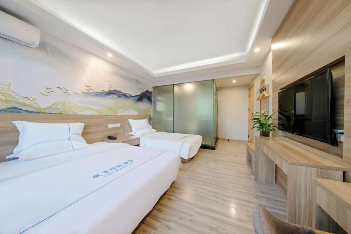 A hotel room with two beds, a TV, a painting on the wall, and a wooden floor.