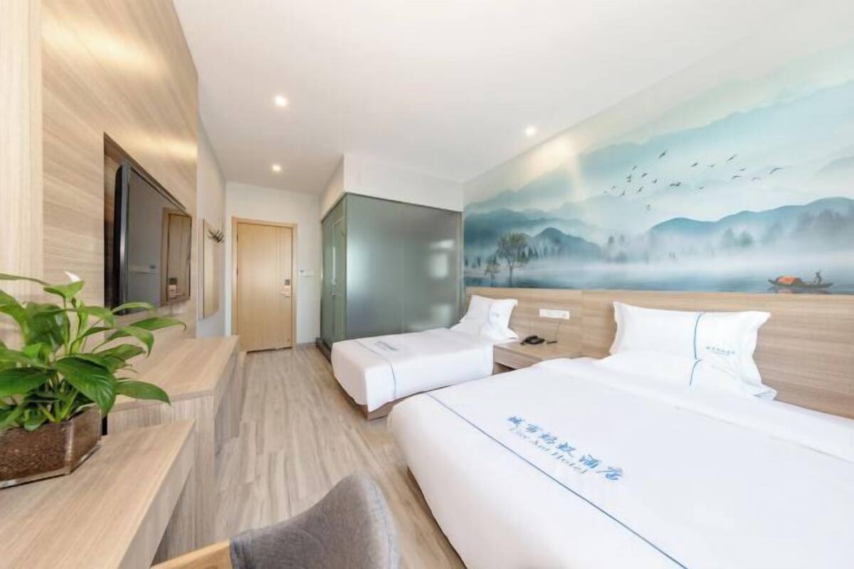 A hotel room with two beds, a desk, a chair, a TV, and a painting of a landscape.