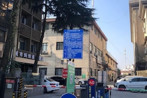 A street view with a blue informational sign, a closed white car, and a building with a sign in a foreign language.