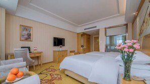 A hotel room with a bed, a desk, a chair, a TV, and a vase of flowers. - Vienna Hotel (Wuhan Central China Normal University, Huquan Metro Station) (Wuhan)