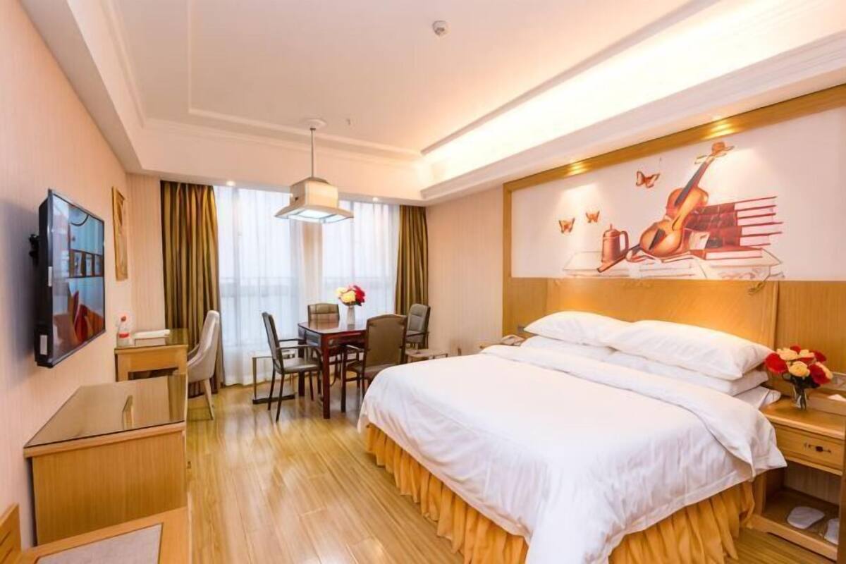Hotellihuone, jossa on sänky, työpöytä, tuoli ja taulu seinällä.