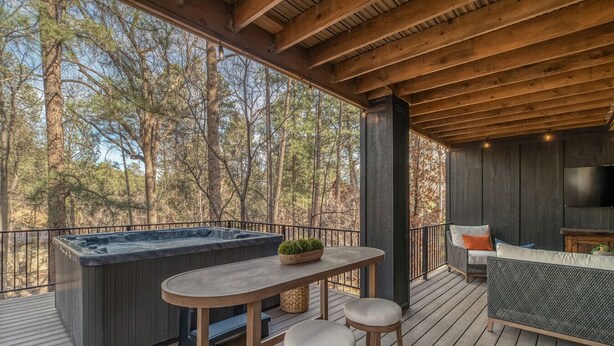 Eine HolzdTerrasse mit Whirlpool, Tisch und Barhocker mit Blick auf ein bewaldetes Gebiet.