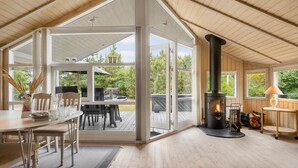 A cozy cabin interior with a dining area, a wood-burning stove, and large windows offering a view of the outdoors. - Gorgeous home in Slagelse with WiFi (Slagelse)
