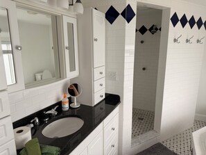 A bathroom with a white sink, mirror, and white cabinets. There is a shower with a black and white tiled wall. - Wake up to spectacular sunrises and the sound of waves at this great beach house (Marshfield)