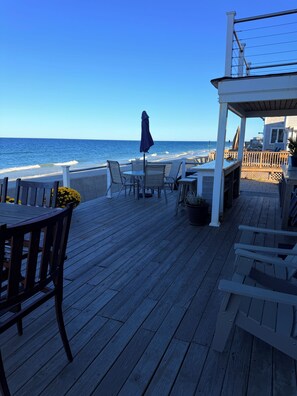 A wooden deck with outdoor seating overlooking the ocean. - Wake up to spectacular sunrises and the sound of waves at this great beach house (Marshfield)