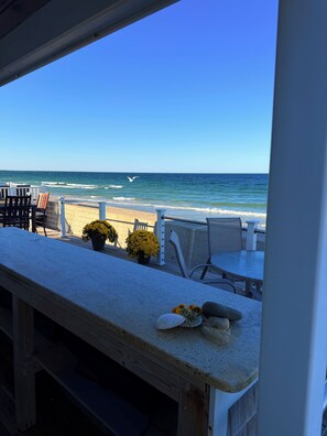 A beachside view with a patio area featuring a table, chairs, and potted plants. - Wake up to spectacular sunrises and the sound of waves at this great beach house (Marshfield)