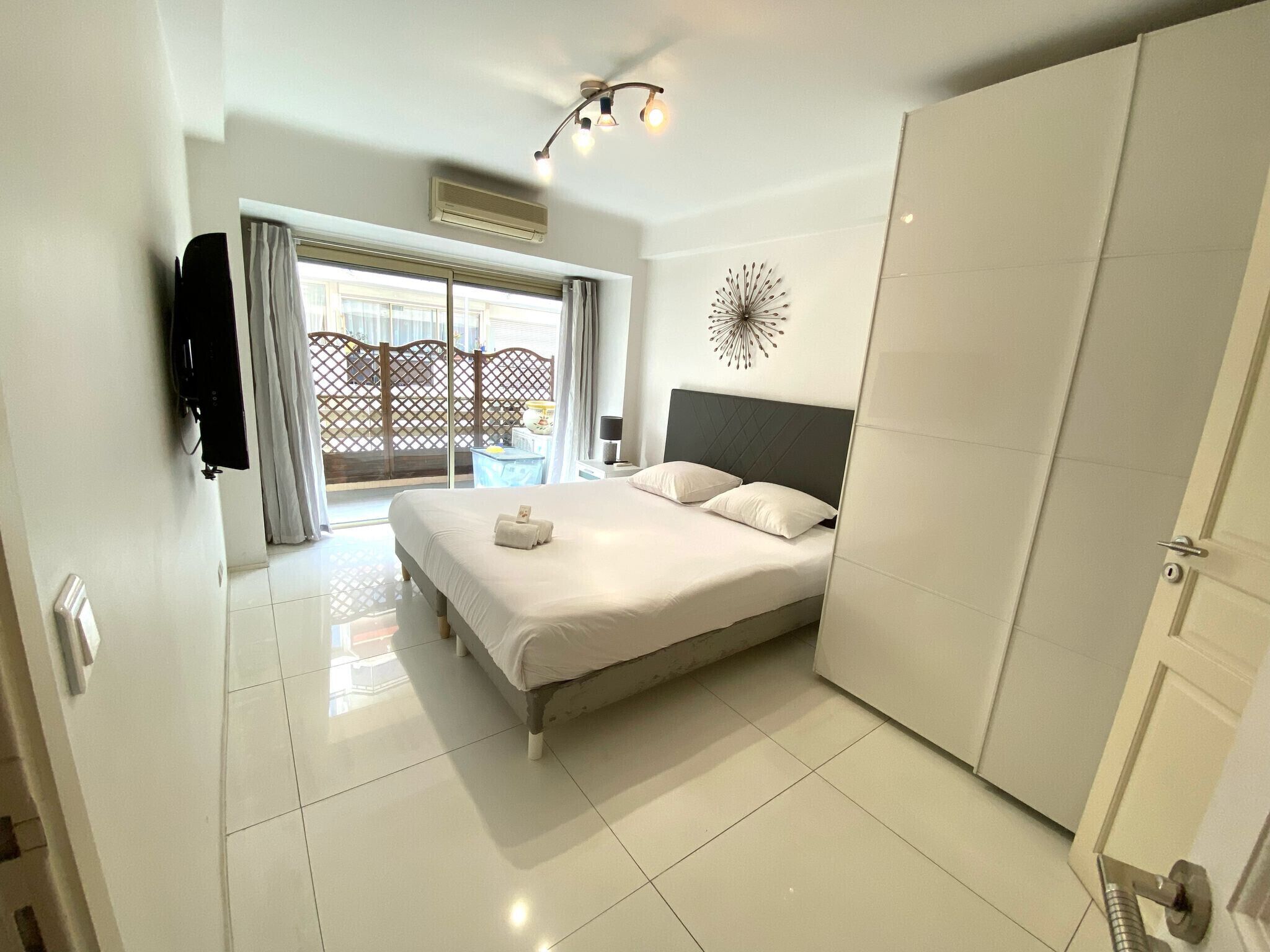 A hotel room with a bed, a wardrobe, a TV, and a view of the outside.