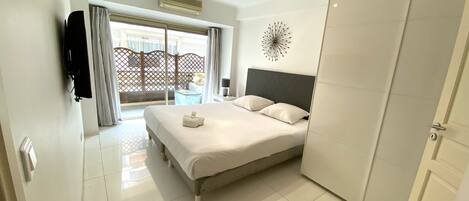 A hotel room with a bed, a wardrobe, a TV, and a view of the outside.
