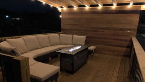 Eine Holzterrasse mit einer gebogenen Couch und einem Feuerkorb.