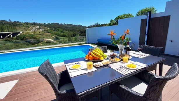 Una mesa de comedor con sillas de mimbre, una piscina y vistas a las colinas.