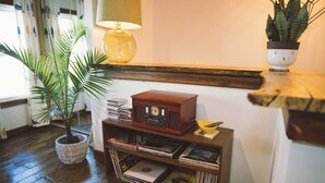 Ein gemütliches Zimmer mit Holzboden, einem Vintage-Radio auf einem Holzständer, einer Topfpflanze und einer Lampe.