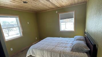 Une chambre avec un plafond en bois, deux fenêtres, un lit et un sol recouvert de moquette.