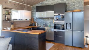 A modern kitchen with dark cabinetry, a central island, stainless steel appliances, and a stone accent wall.