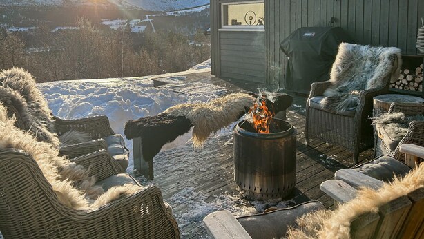A cozy outdoor seating area with a fire pit, wicker furniture, and a view of a snowy landscape.