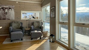 A cozy living room with two grey armchairs, a small table, and a large window offering a snowy mountain view.