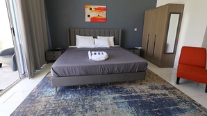 A modern bedroom with a large bed, a grey headboard, a blue and beige patterned rug, a red chair, and a wooden wardrobe. - Pàris Villas Modern Suite (Gros Islet)