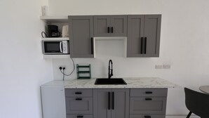 A compact kitchen with grey cabinets, a built-in microwave, and a sink. - Pàris Villas Modern Suite (Gros Islet)