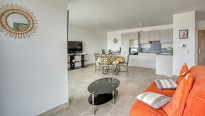 A modern apartment with a living room featuring a sofa and a coffee table, a dining area with a table and chairs, and a kitchen with a stove and cabinets. - Amazing apartment in La Tremblade with WiFi (La Tremblade)