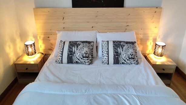 Un dormitorio con un cuadro grande de un león en la pared, cabecera de madera, ropa de cama blanca y dos lámparas de noche.