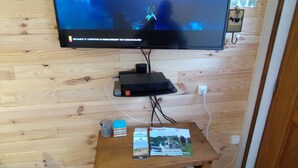 Un televisor montado en una pared de madera, un mueble de madera debajo y una mesita con una revista y un vaso.